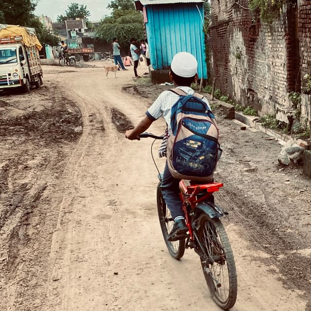 A kid cycling to along a dusty rural road.